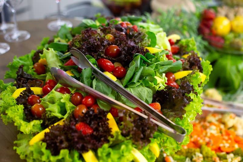 Fresh mixed greens salad with cherry tomatoes, colorful vegetables, and serving tongs on a wooden surface