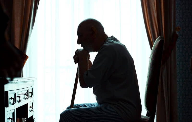 An older person looking out a window alone