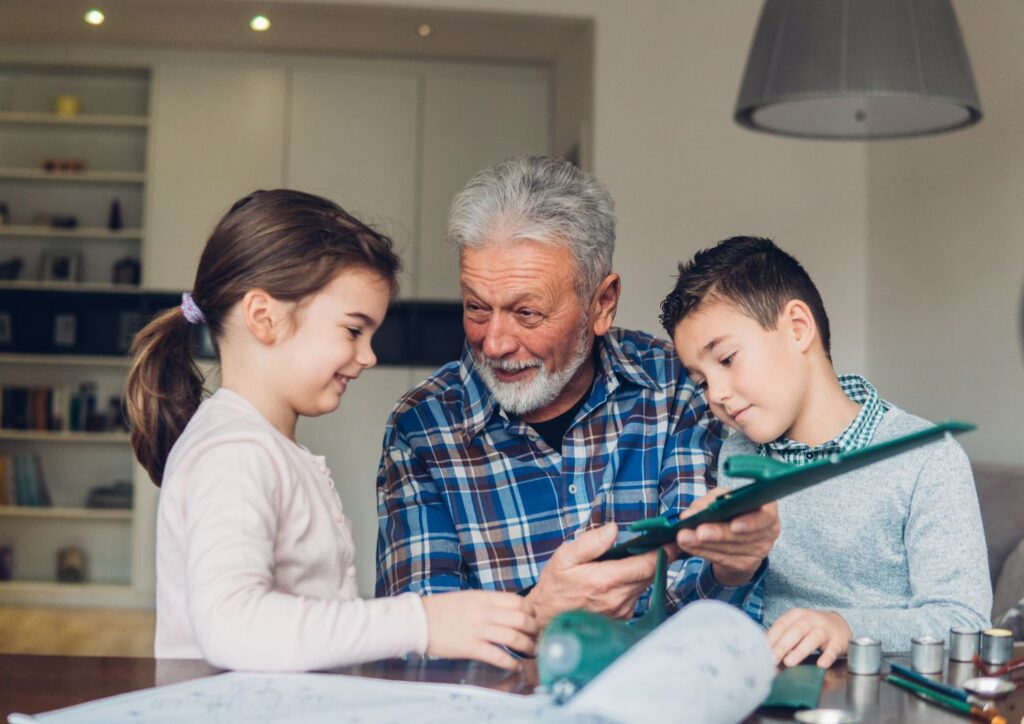 Grandfather and two grandchildren working together on a craft project at a kitchen table