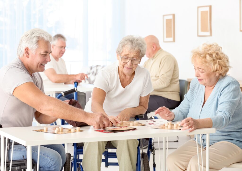 Seniors playing board games together at a table in a bright community room, enjoying social activities and recreation